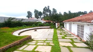Um pátio com um caminho de pedra curvo, área gramada e um edifício branco com telhado de telhas vermelhas.