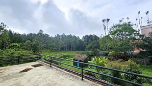 Um terraço de concreto com grades de metal, rodeado por vegetaç ão exuberante e árvores.