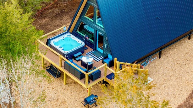 Een modern, A-frame huis met een hottub en een terras.