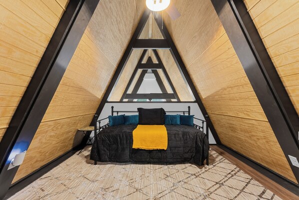 Une pièce triangulaire comprenant un lit, une petite table et une chaise.
