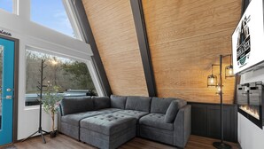 Een moderne woonkamer met een hoekbank, een vloerlamp en uitzicht op de natuur.