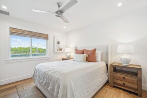 A bedroom with a large bed, a ceiling fan, a window with a view, two bedside tables with lamps, and a wooden nightstand. - Private Beach Access, Private Pool/Hot Tub, Beach Service, and Pet Friendly! (Santa Rosa Beach)