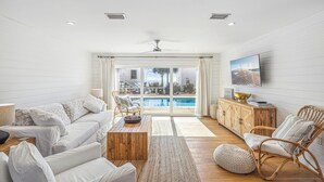 A modern living room with a white sofa, wooden coffee table, wicker chairs, and a view of a pool through large glass doors. - Private Beach Access, Private Pool/Hot Tub, Beach Service, and Pet Friendly! (Santa Rosa Beach)