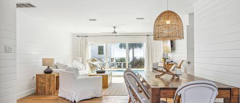 A spacious room with a wooden dining table, wicker chairs, and a large window overlooking a pool.