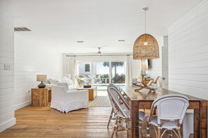 Una habitación amplia con una mesa de comedor de madera, sillas de mimbre y un gran ventanal con vistas a una piscina.