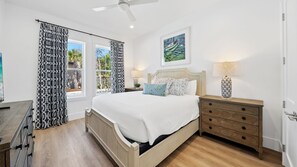A bedroom with a bed, bedside tables, a ceiling fan, and a window with patterned curtains.