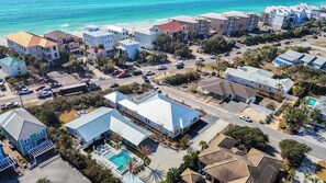 An aerial view of a coastal residential area with houses, a swimming pool, and a beach.
