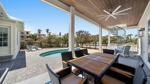 A covered outdoor area with a pool, wicker furniture, and a spiral staircase.