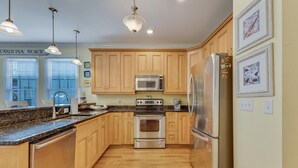 A modern kitchen with wooden cabinets, stainless steel appliances, and pendant lighting.