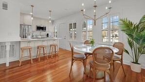 Una cocina moderna con armarios blancos, electrodomésticos de acero inoxidable y una zona de comedor con sillas de mimbre y una mesa redonda.
