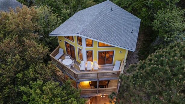 Une maison à deux étages dotée d’une terrasse, entourée d’une forêt dense.