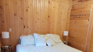 Um quarto com painéis de madeira, uma cama, duas luminárias de cabeceira e um tapete estampado.