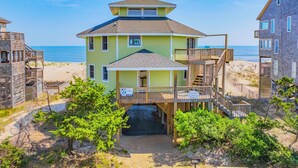 A beachfront property with a two-story house, a covered porch, and a wooden deck. - Oceanfront Home in Avon with Hot Tub, Grill, Smart TVs. Pure Beachfront Bliss! (Avon)