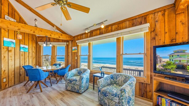 A wooden interior with a dining area, two patterned armchairs, a ceiling fan, and a television. - Oceanfront Home in Avon with Hot Tub, Grill, Smart TVs. Pure Beachfront Bliss! (Avon)