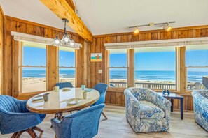 Quarto com decoração em madeira, grandes janelas com vista para a praia, mesa redonda com cadeiras e um sofá estampado.