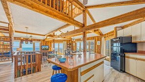 A spacious cabin interior with a wooden interior, a kitchen area, and a dining space with a view. - Oceanfront Home in Avon with Hot Tub, Grill, Smart TVs. Pure Beachfront Bliss! (Avon)