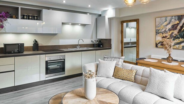 A modern kitchen with white cabinets, a built-in oven, and a microwave. There's a dining area with a wooden table and a sofa. - Host & Stay | Chic Townhouse by the Docks (Liverpool)