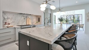 A modern kitchen with a marble countertop, a built-in stove, and a large island with bar stools. - 2 Min Walk to Beach, Bikes, Paddleboards, Heated Pool, Hot Tub, Fireplace (Holmes Beach)
