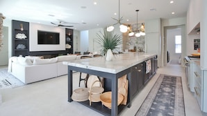 A modern kitchen with a central island, built-in appliances, and a large TV. - 2 Min Walk to Beach, Bikes, Paddleboards, Heated Pool, Hot Tub, Fireplace (Holmes Beach)