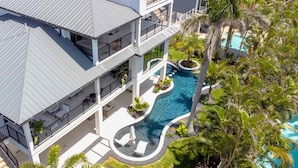 A multi-story building with a swimming pool, outdoor seating, and lush landscaping. - 2 Min Walk to Beach, Bikes, Paddleboards, Heated Pool, Hot Tub, Fireplace (Holmes Beach)
