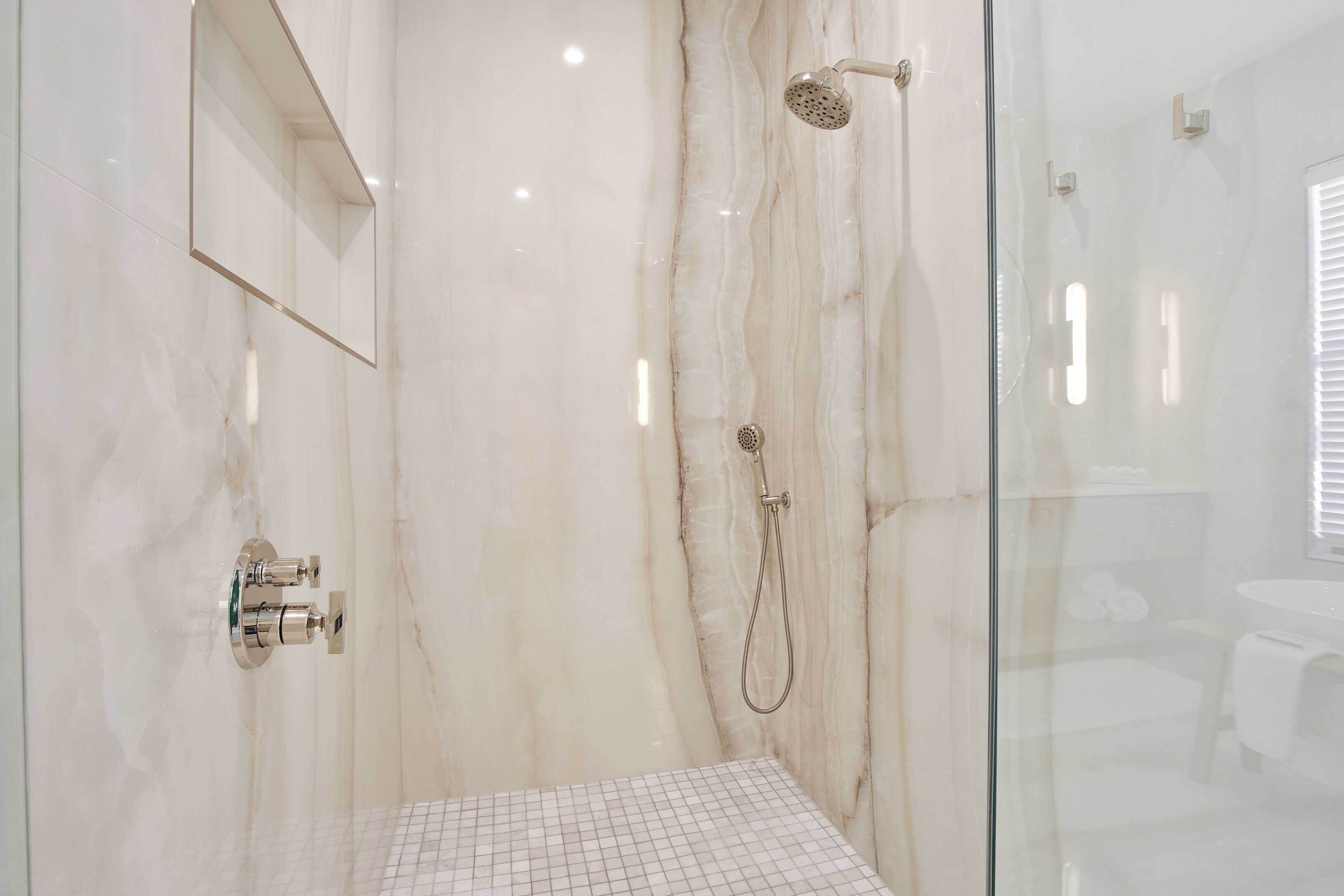 A modern bathroom with a glass shower enclosure, marble walls, and a grid-patterned floor.