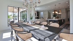 A modern dining area with a large wooden table, wicker chairs, and hanging light fixtures. - 2 Min Walk to Beach, Bikes, Paddleboards, Heated Pool, Hot Tub, Fireplace (Holmes Beach)
