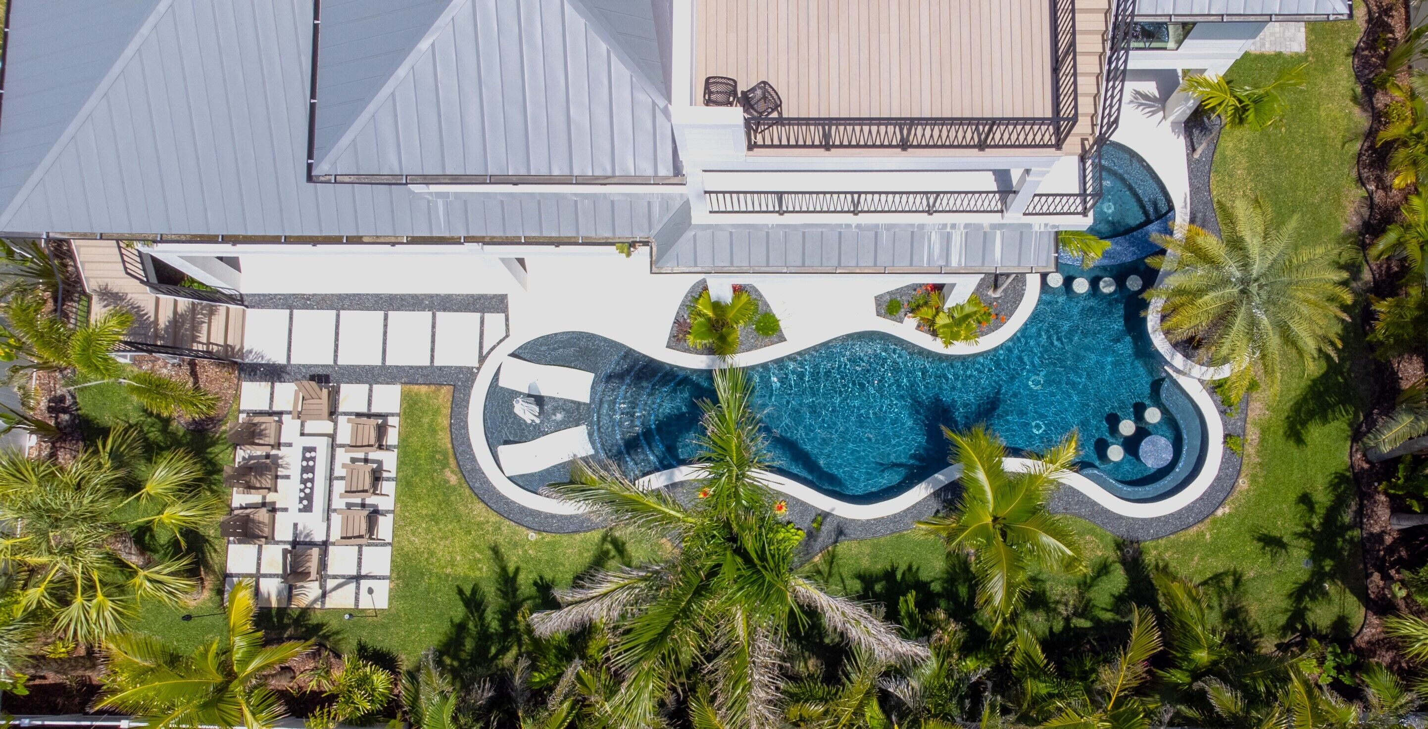 An aerial view of a resort with a large swimming pool, lounge area, and lush tropical landscaping.