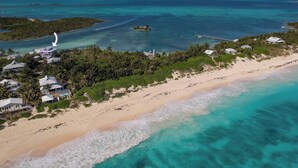 Vista aérea de uma área costeira com praia de areia, águas turquesa cristalinas e uma pequena ilha com um farol.