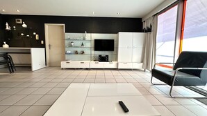 Ein modernes Wohnzimmer mit einer weißen Unterhaltungsecke, einem Flachbildfernseher und einem schwarzen Ledersofa.