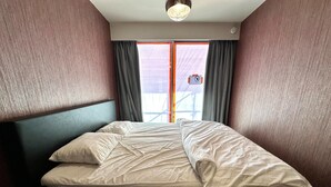 Ein Einzelbett in einem Raum mit Holz-Kopfteil, einem fenster mit Vorhängen und Blick auf einen Balkon.