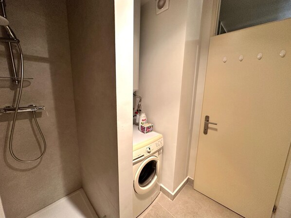 Une petite salle de bain comprenant une douche, un lave-linge et des toilettes.