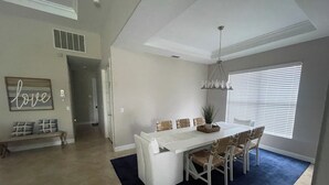 A dining area with a white table and chairs, a dark blue rug, and a chandelier. - Beautiful 3-bedroom house in a gated community in Estero. Pool, Spa, Fitness (Fort Myers)