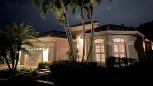A well-lit, two-story house with a garage, surrounded by palm trees and a landscaped garden. - Beautiful 3-bedroom house in a gated community in Estero. Pool, Spa, Fitness (Fort Myers)
