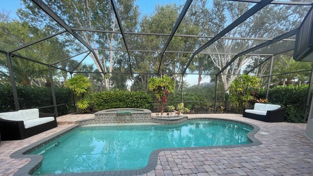 A swimming pool with a brick patio, surrounded by a covered area with two white cushioned seating areas. - Beautiful 3-bedroom house in a gated community in Estero. Pool, Spa, Fitness (Fort Myers)