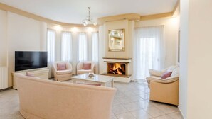 A modern living room with a flat-screen TV, two armchairs, a sofa, a coffee table, and a fireplace. - Villa Amare - Heraklion Private Pool & Garden Gem (Kato Gouves)