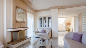 A spacious living room with a fireplace, a glass coffee table, and a sofa. - Villa Amare - Heraklion Private Pool & Garden Gem (Kato Gouves)