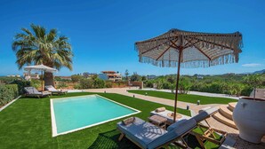 A pool with lounge chairs, a palm tree, and a view of houses in the background. - Villa Amare - Heraklion Private Pool & Garden Gem (Kato Gouves)