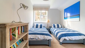 A bedroom with two beds, a bookshelf, a window with a view, and a painting on the wall.