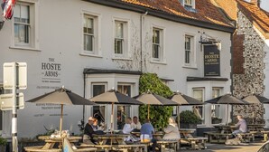 An outdoor seating area of The Hoste Arms with wooden tables and umbrellas.