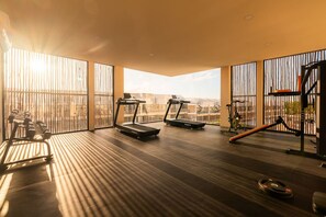 Une salle de sport équipée de tapis de course, d’haltères et d’un vélo d’appartement, avec de grandes fenêtres donnant sur des immeubles.