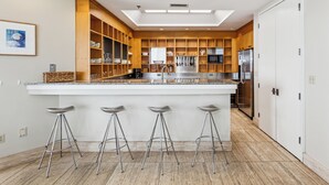 Une cuisine moderne dotée d’un îlot central, d’appareils électroménagers en acier inoxydable, d’étagères en bois et d’une lucarne.
