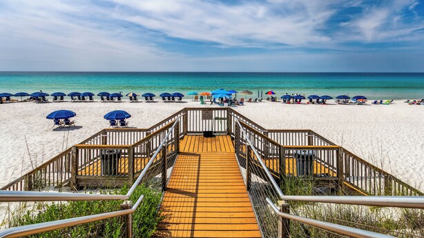 Une promenade en bois menant à une plage agrémentée de parasols et de chaises longues.