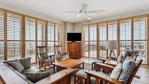 Un vaste espace de vie comprenant une grande table en bois, des sièges confortables, un ventilateur de plafond et un téléviseur.