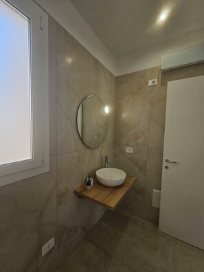 A bathroom with a round mirror, a white sink on a wooden shelf, and a white door.