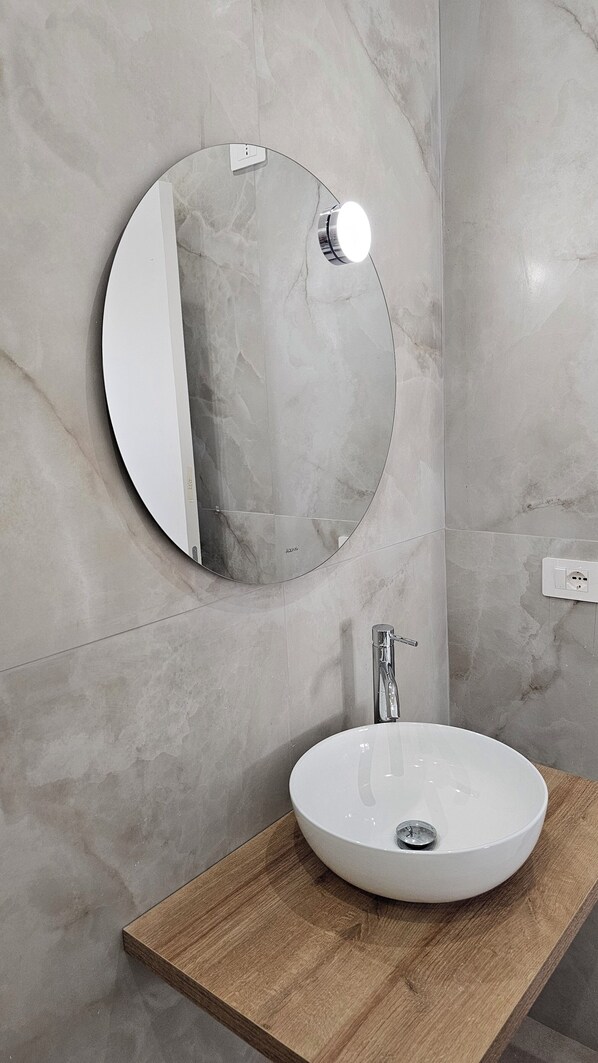 A bathroom with a round mirror, a white sink, and a wooden countertop.