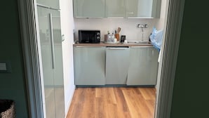 Une cuisine moderne avec des meubles de couleur vert clair, un plancher en bois et un luminaire suspendu.