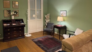 Un salon avec une commode en bois foncé, un fauteuil gris, un canapé beige, un tapis à motifs et une porte blanche avec des panneaux de verre.