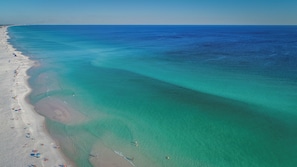 Et luftfoto af en strand med klart turkis vand, sandet bredde og parasoller.