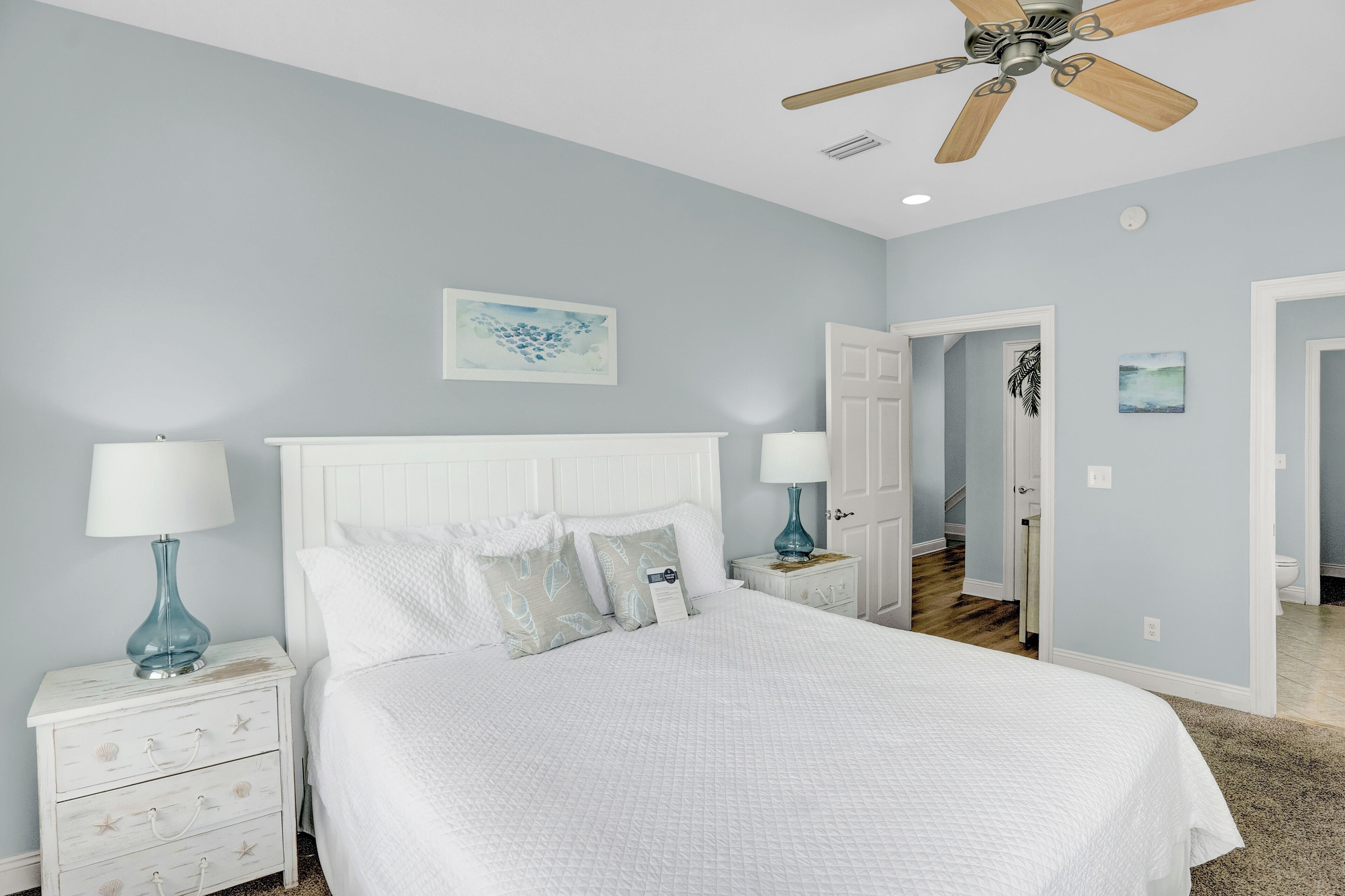 A bedroom with a bed, nightstands, a ceiling fan, and artwork on the walls.