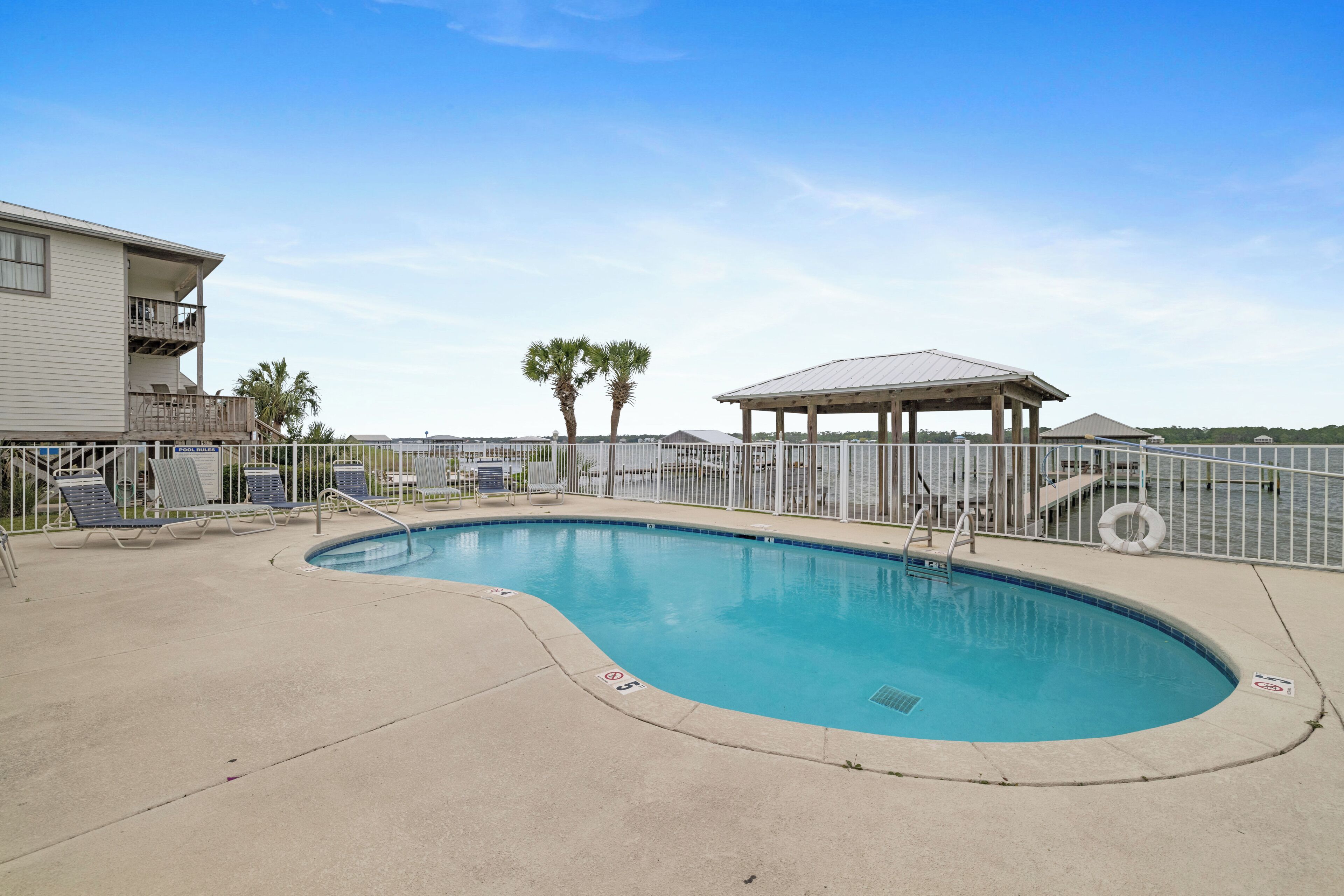 A swimming pool with lounge chairs, a covered pavilion, and a building with a balcony.